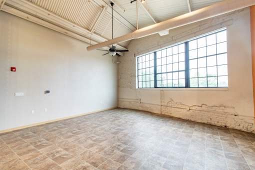 A large empty room with a ceiling fan and a window.