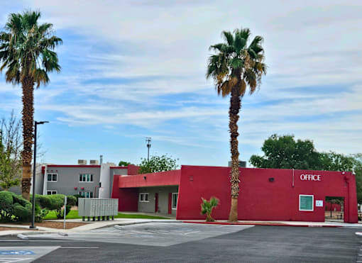 A red building with the word "OFFICE" on it is surrounded by palm trees.