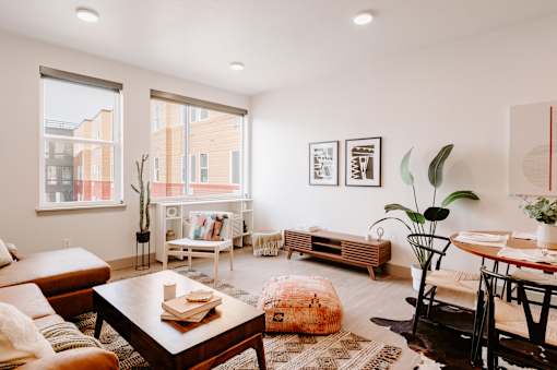 A living room with a brown leather couch, a wooden coffee table, and a large window with a view of a building outside.