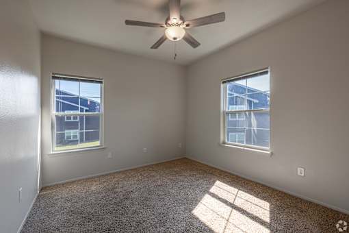 A room with a ceiling fan and two windows.