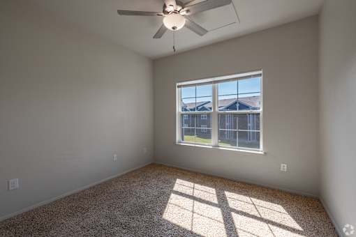 A room with a ceiling fan and a window overlooking a fenced area.
