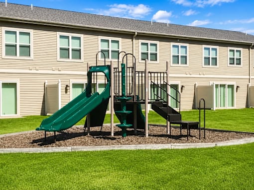 A playground with a green slide and a black slide in front of a building.