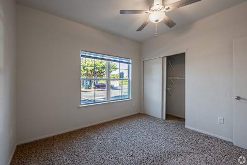 A room with a ceiling fan and a window overlooking a street.