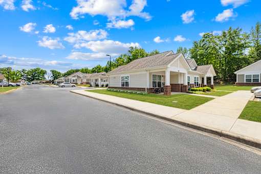 A street view of a residential area with houses on the right and a clear blue sky above.