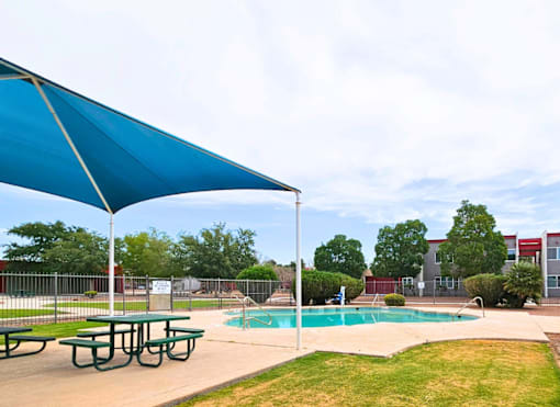 A blue umbrella is over a picnic table next to a pool.