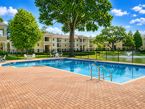 A swimming pool surrounded by a brick patio and a black fence with a building in the background.