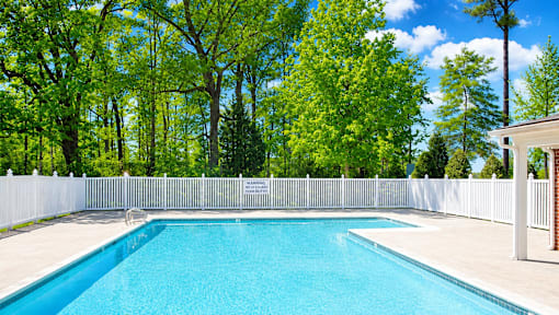 A swimming pool surrounded by a white fence and trees.