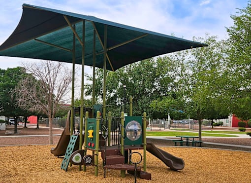 A playground with a green canopy and a slide.