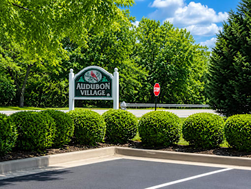 A sign for Audubon Village stands in front of a row of bushes.