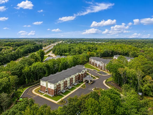 A large building surrounded by trees with a parking lot in front.