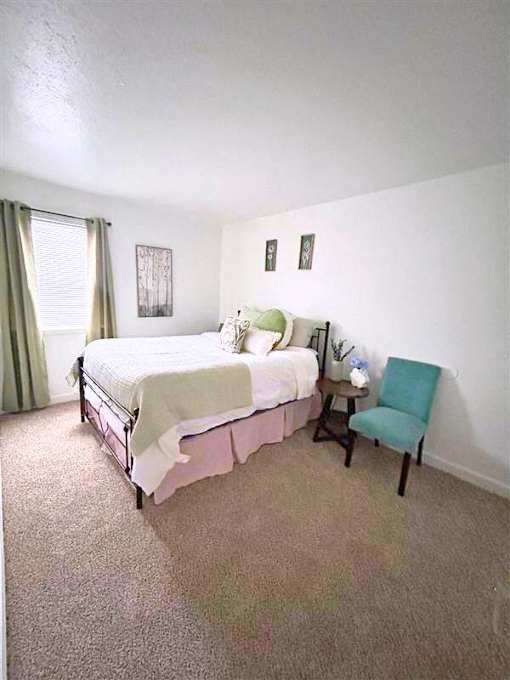 A bedroom with a bed, chair, and pictures on the wall.