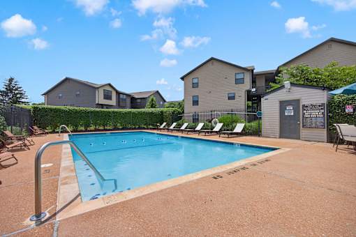 A pool surrounded by chairs and a fence with a building in the background.