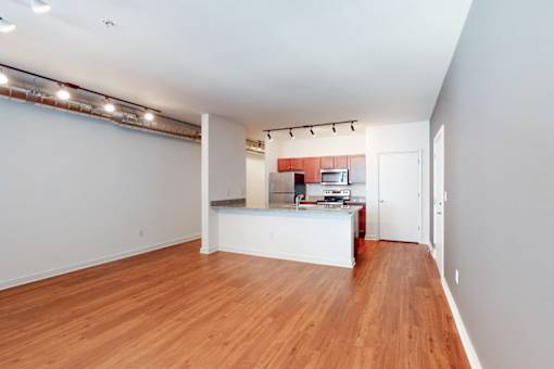 A room with wooden floors and a kitchen area in the background.