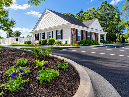 A white building with a black roof and a flower bed in front of it.