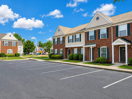 A parking lot in front of a brick building with a blue sky and clouds in the background.