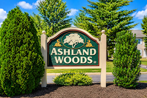 A sign for Ashland Woods is displayed in front of some trees.