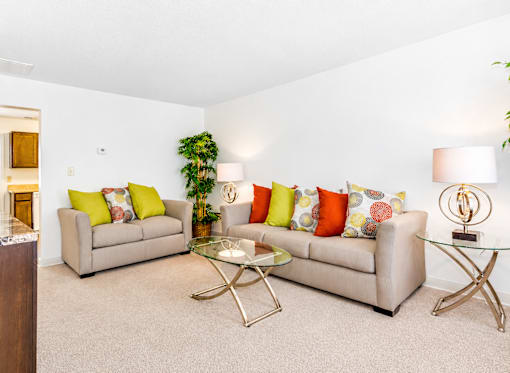 A living room with a beige couch, a glass coffee table, and a plant.