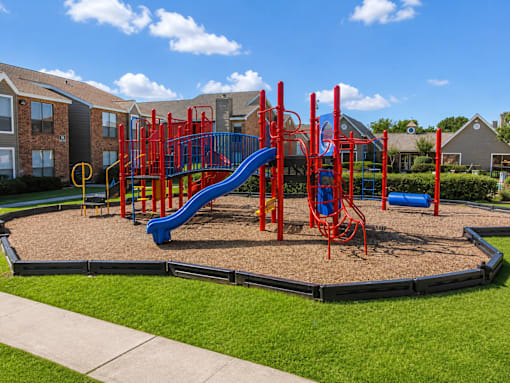 A playground with a red and blue slide and a yellow circle on the ground.