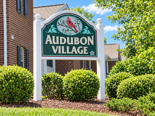 A sign for Audubon Village stands in front of a building.