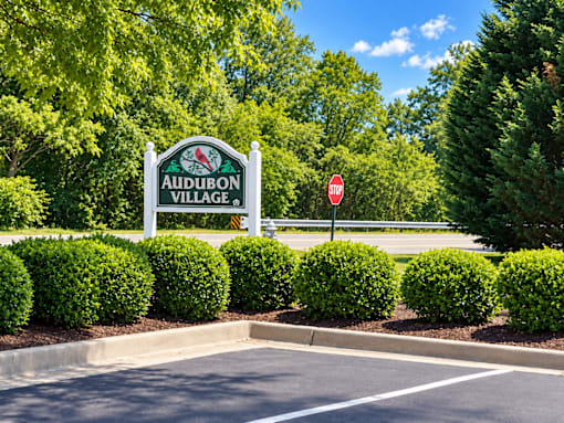 A sign for Audubon Village stands in front of a parking lot.