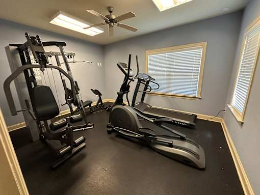 the gym has plenty of exercise equipment and a ceiling fan