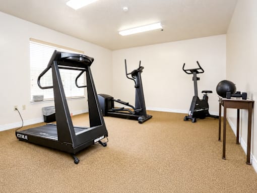 A room with a treadmill, two stationary bikes, and a ball.