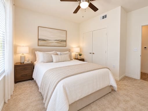 A bedroom with a large bed, two lamps, and a painting on the wall.