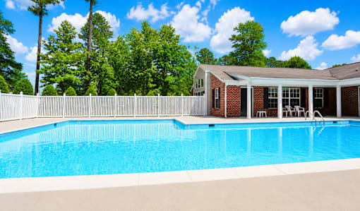 A pool in front of a house with trees in the background.