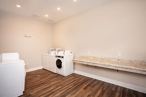 A white dryer and washing machine in a room with wood flooring.