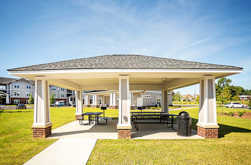 A pavilion with a roof and pillars is surrounded by a grassy area.