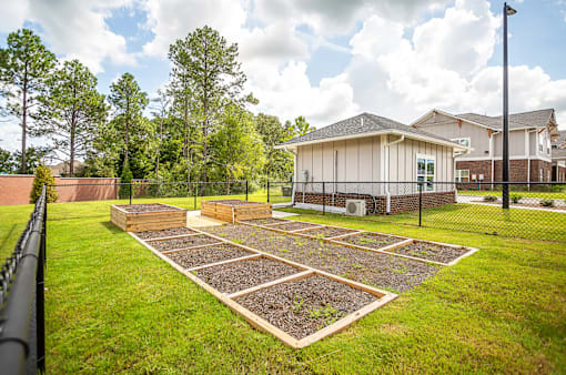 A garden with a fence and a house in the background.