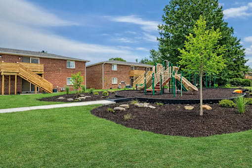 A playground with a green slide and a tree in the foreground.