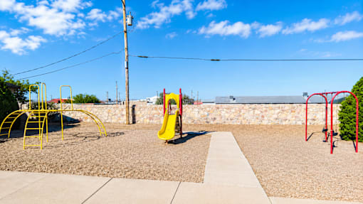 A playground with a yellow slide and red swings.