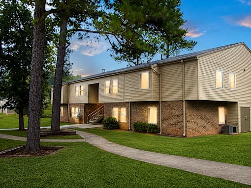 A building with a brown siding and a brick wall is surrounded by a grassy area and trees.