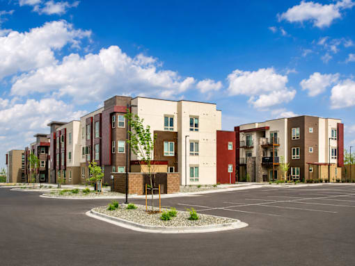 A row of modern apartment buildings with a parking lot in front.