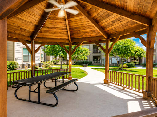 A wooden pavilion with a ceiling fan and two benches.