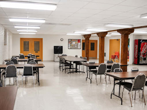 A room with tables and chairs and a TV on the wall.