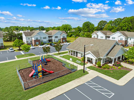 A playground with a slide and swings is surrounded by a fence and a parking lot.