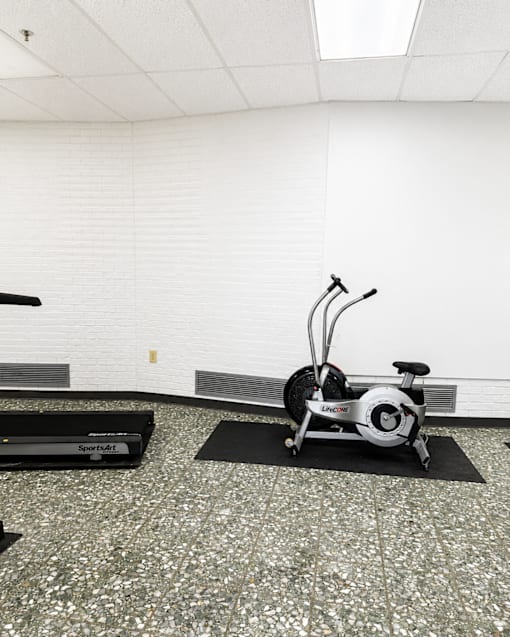 A stationary bike is on a black mat in a room with a white wall.