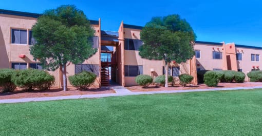 an apartment building with a lawn and trees in front of it