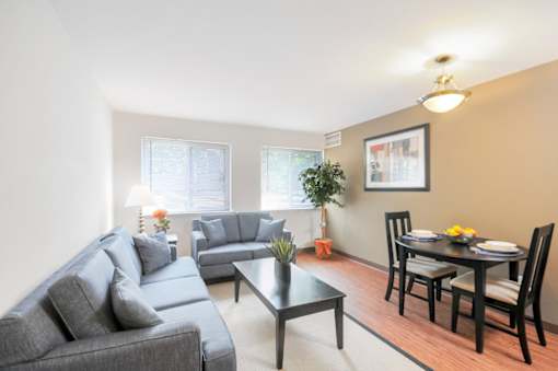 A living room with a grey couch, a black coffee table, and a dining table set for two.