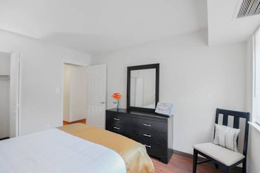 A bedroom with a bed, dresser, mirror, and chair.