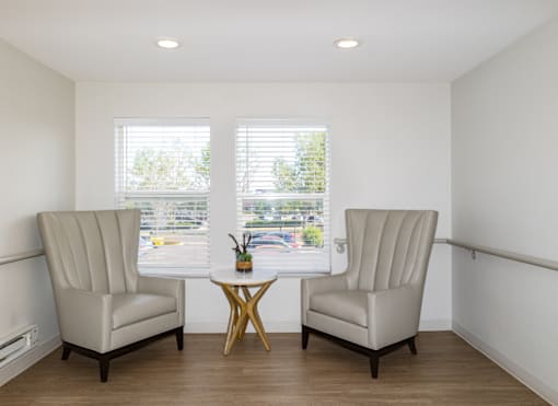 Two chairs and a table are in a room with windows.