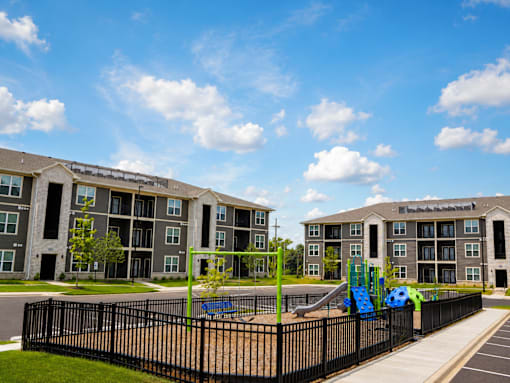 A playground with a slide is in front of apartment buildings.