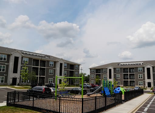 A playground with a slide and a green climbing frame is in front of apartment buildings.