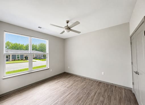 A room with a ceiling fan and a window overlooking a parking lot.