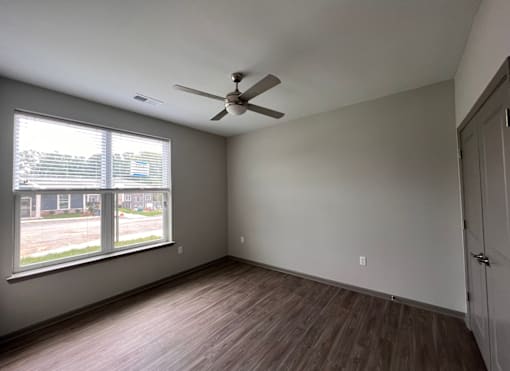 A room with a ceiling fan and a window overlooking a parking lot.