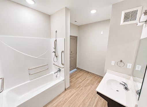 A white bathroom with a wooden floor and a white tub.