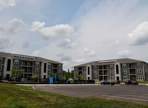 Two apartment buildings with a parking lot in front.