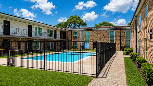 A black fence surrounds a small pool in a sunny backyard.